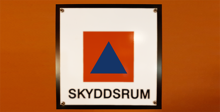 Foto: Skylten skyddsrum, orange fyrkant med blå trekant med texten Skyddsrum under